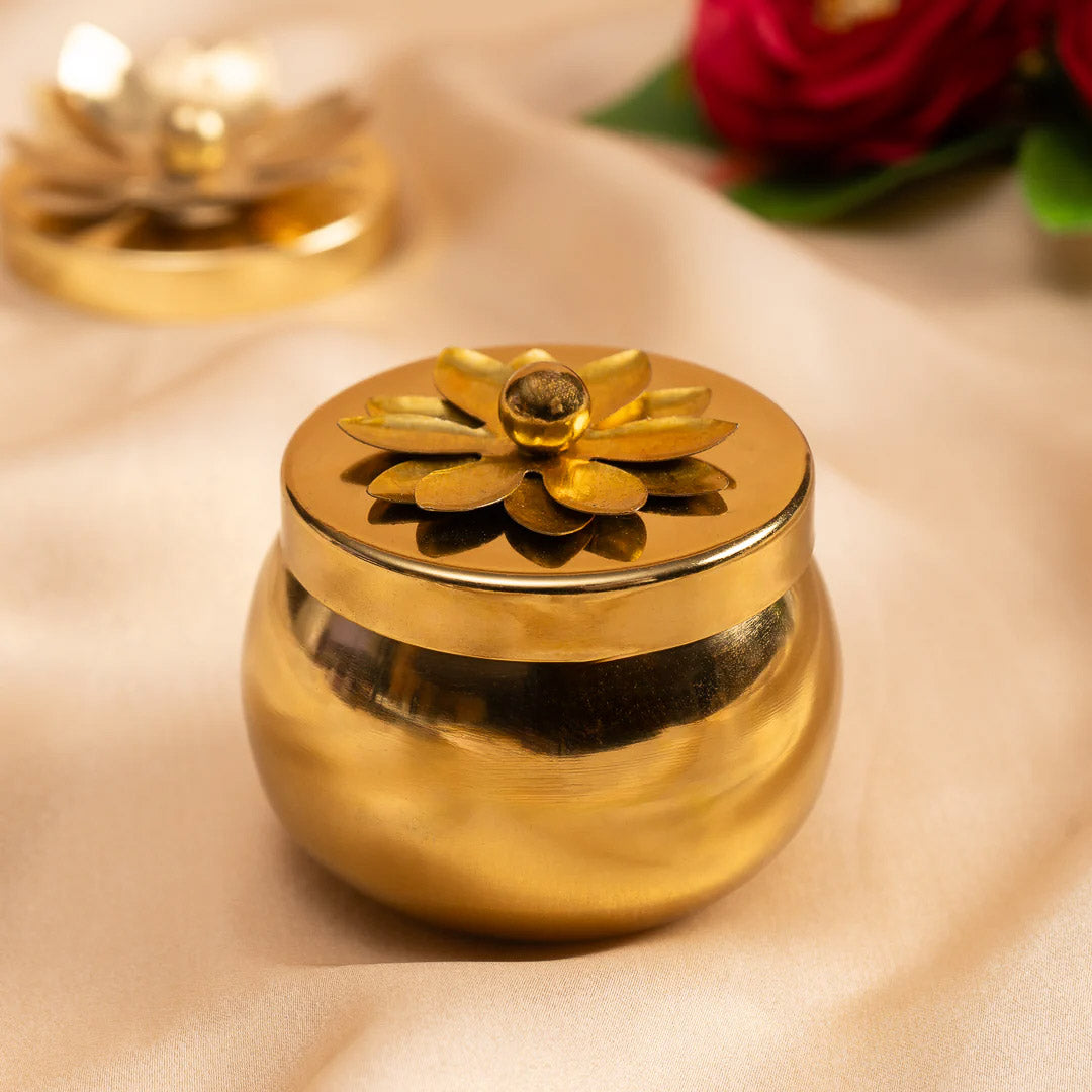 Gold decorative pot with a lid featuring a floral design on a beige surface.