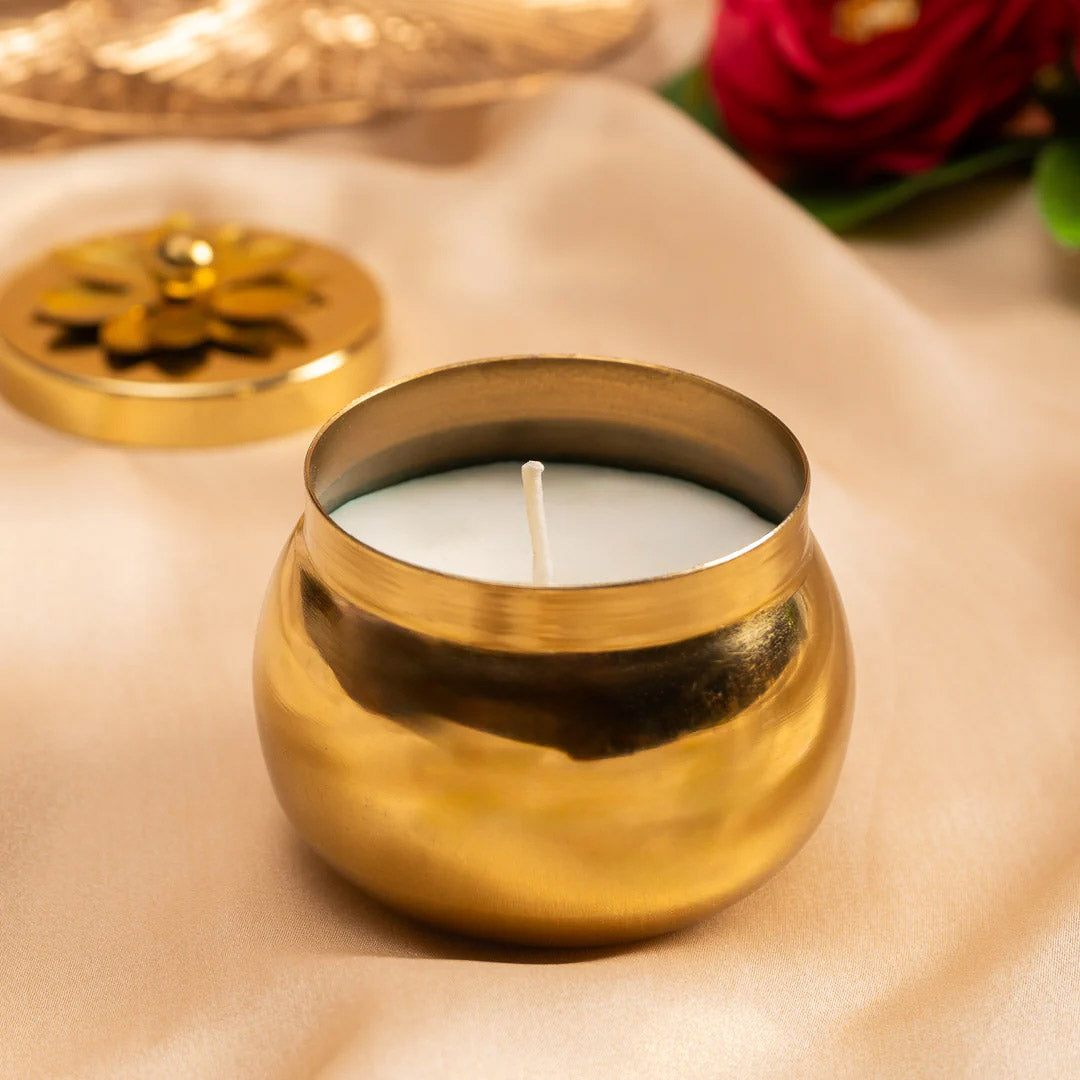 Gold candle holder with a lit candle on a beige surface