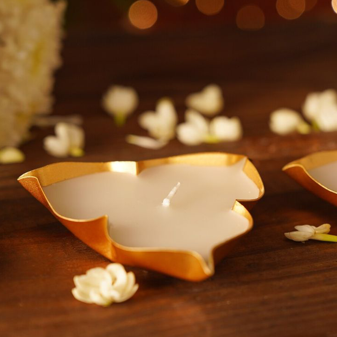 Decorative leaf-shaped candles on a wooden surface with blurred lights in the background